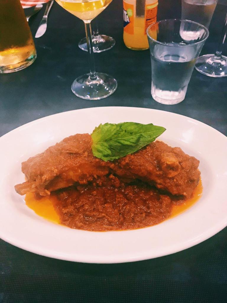 A rib on a white plate with the Naples Ragu sauce over it, and a basil leaf on top. 
