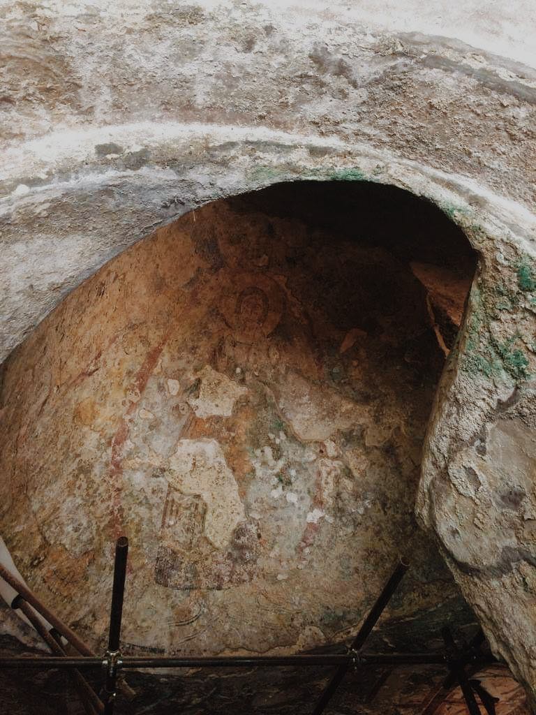 Fresco painting of Christ in an alcove with scaffolding around it, in the San Gennaro Catacombs.