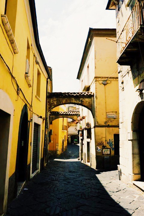 Street in Benevento Campania. With yellow buildings either side and arches between buildings.
