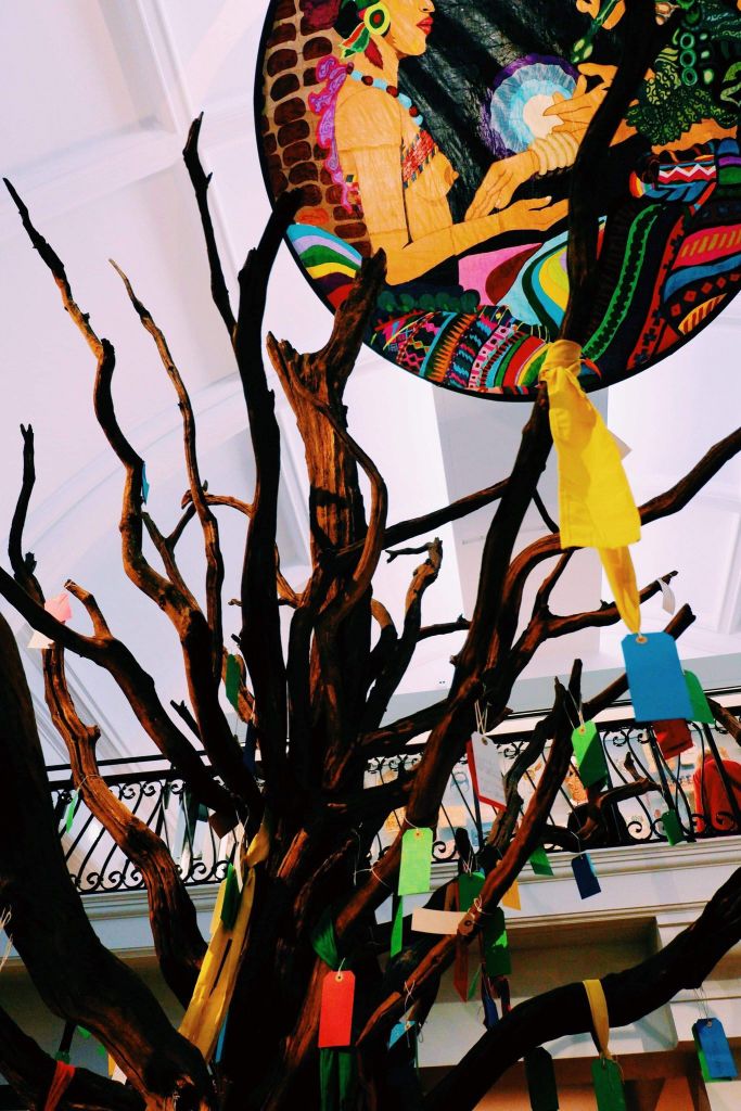 Tree in the centre of the World Gallery in the Horniman Museum with colourful ties and notes hanging off the wooden branches.