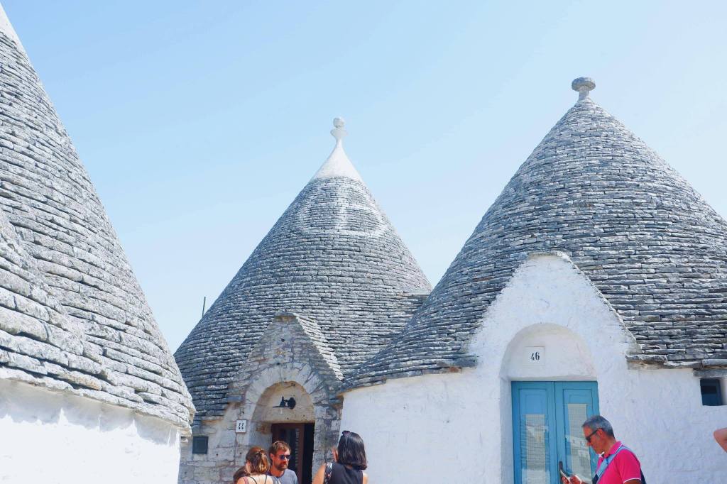 Stone rooms of Trulli in Alberobello. Three trulli are beside one another, the middle one has a white painted symbol and a pinnacle on top.