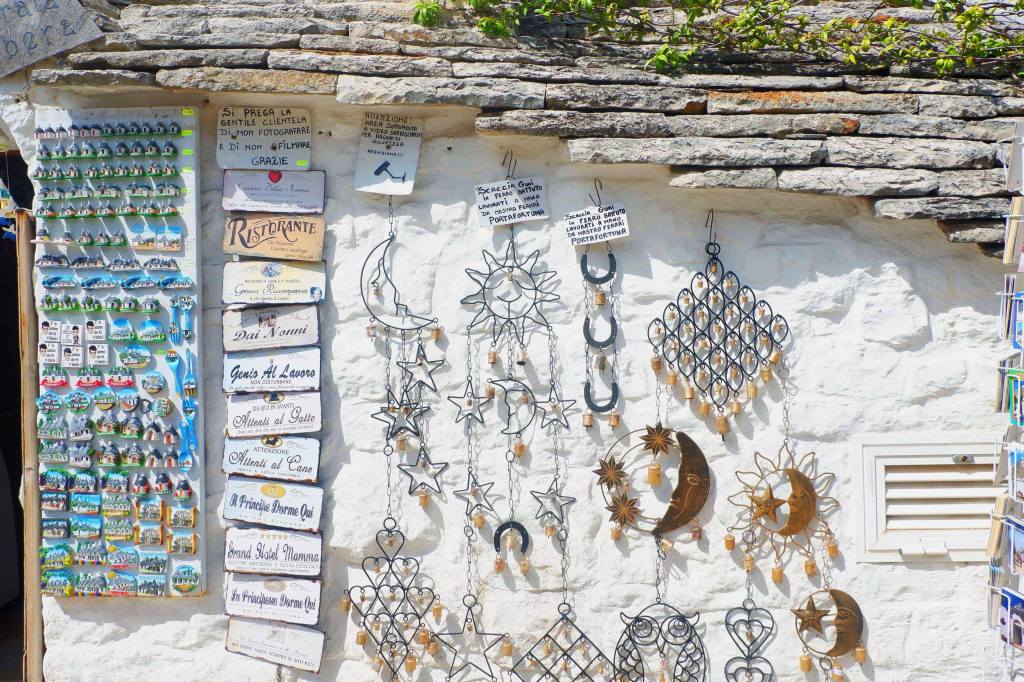 A gift shop in a trulli in Alberobello. Blue magnets hang down the left hand side, beside are house signs along, along most of the wall are wind chimes in the shape of moon, sun, stars, hearts. 