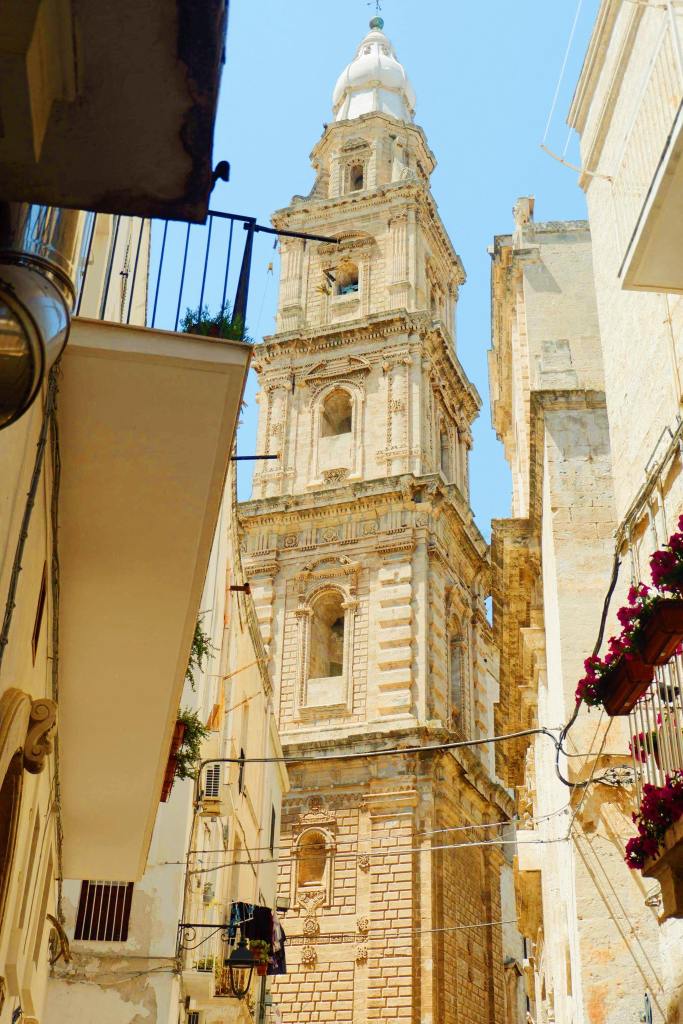 Church in Monopoli, Puglia. The church is centre of the image with blue skies. Yellow buildings are either side of the street, leading to the church.