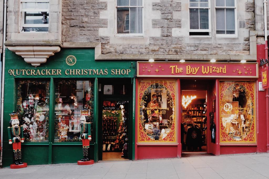 Storefronts on the Royal Mile. On the left is the Nutcracker Christmas Shop in green with two nutcrackers at the windows on the right is the Boy Wizard in red with Harry Potter march in the windows