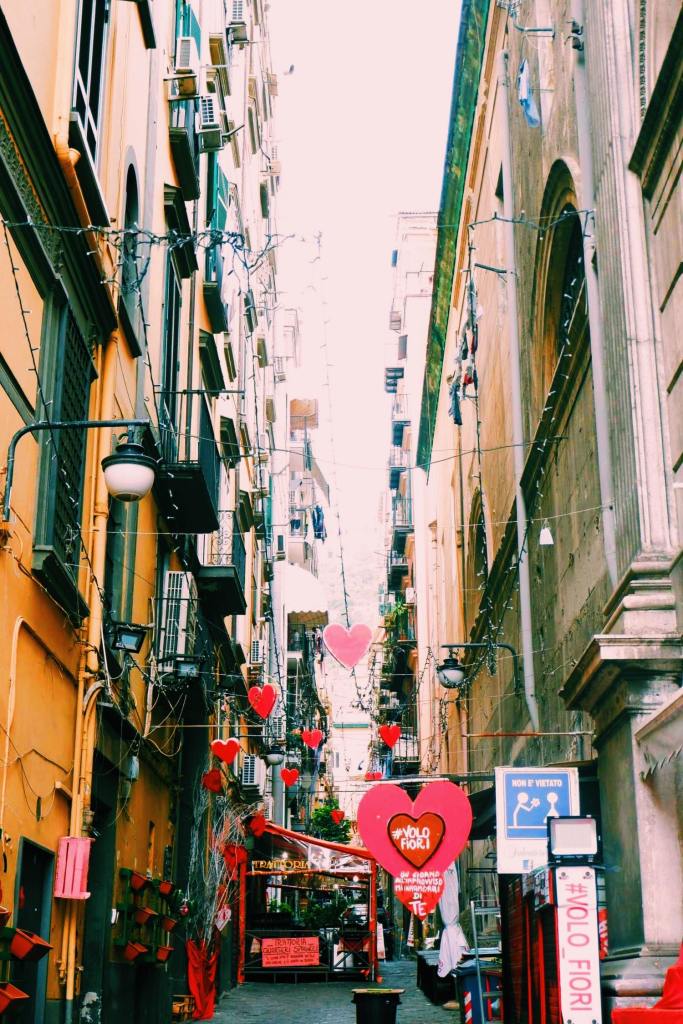 Street in the Spanish quarter of Naples. Between the buildings are red hearts with #volofiori 