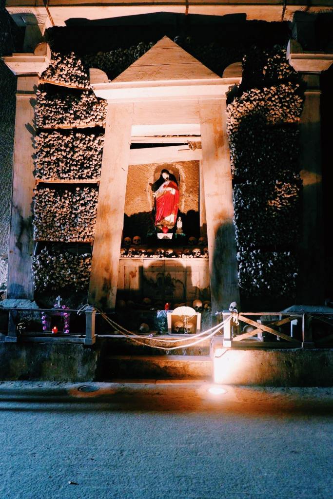 Cimitero Delle Fontanelle. Shrine of long bones and skulls with a statue of Christ lit in the centre. 