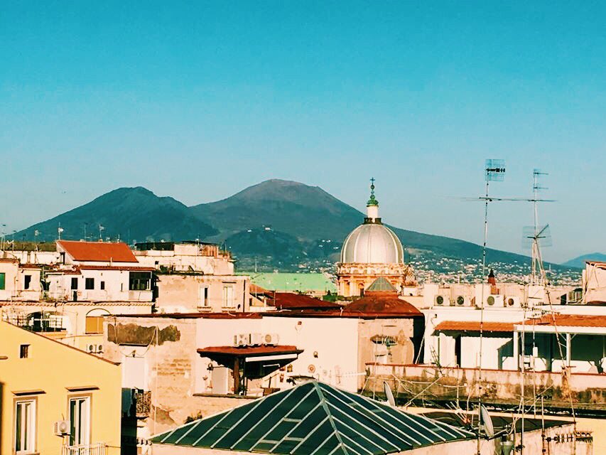 View from a roof top in Naples with buildings across the lower third and Vesuvius behind with a blue sky.